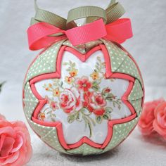 an ornament decorated with flowers and ribbon on a table next to pink roses