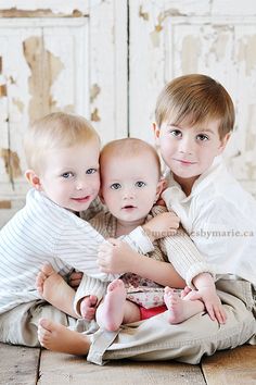 three young children are sitting on the floor and posing for a photo with their arms around each other