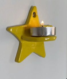 a yellow star shaped candle holder with a silver ring on it's end and a white wall in the background