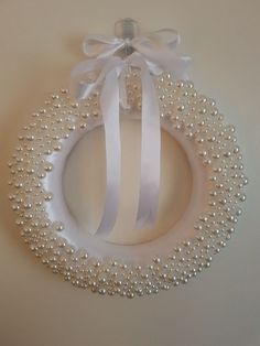 a white wreath with pearls and ribbon hanging on the wall