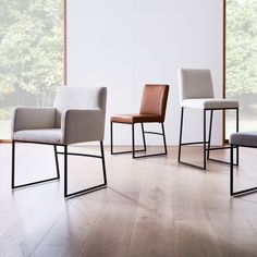 three modern chairs sitting on top of a hard wood floor next to a large window