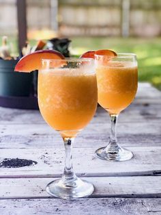 two glasses filled with orange juice sitting on top of a wooden table