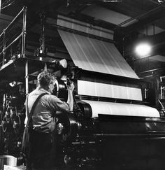 a black and white photo of a man working on a large machine in a factory