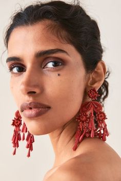 a woman wearing large red earrings with tassels on her neck and shoulder, looking off to the side