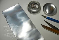 some scissors and other items are laying out on a white table top with silver foil