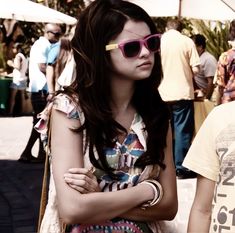 a woman with her arms crossed standing next to a man wearing sunglasses and holding a purse