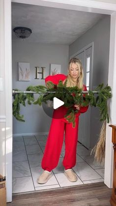 a woman in red pants holding a christmas wreath