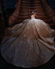 a woman in a ball gown sitting on the stairs with her back to the camera