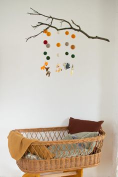 a wicker baby crib in front of a tree branch with balls hanging from it