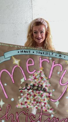 a woman holding up a merry little christmas sign