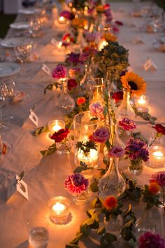 a long table with candles and flowers in vases on top of the tablescloth