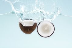 two halves of coconuts with water splashing over them on a light blue background