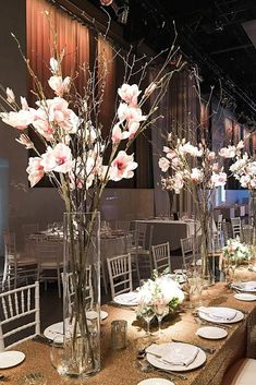 the tables are set with white plates and vases filled with pink flowers on them