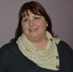 a woman with brown hair wearing a gray sweater and a white knit cowl around her neck