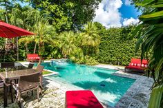 an outdoor swimming pool surrounded by trees and chairs with red umbrellas on the side