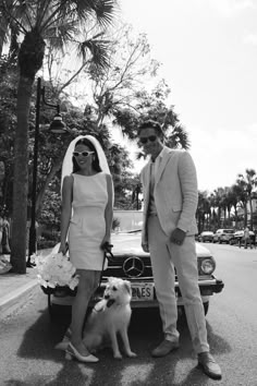 a man and woman standing in front of a car with a dog on the street