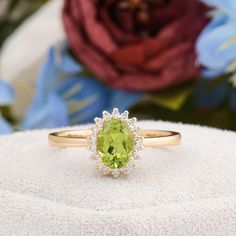 an oval cut peridot and diamond ring sits on a white surface with flowers in the background