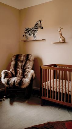 a baby's room with a chair, crib and stuffed zebras on the wall