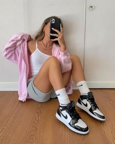 a woman sitting on the floor taking a selfie with her cell phone while wearing nike sneakers