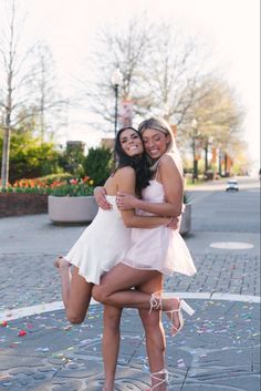 two young women hugging each other on the street with confetti all around them