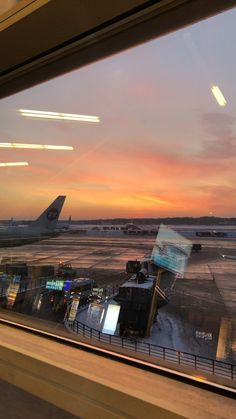 an airplane is sitting on the runway at sunset as seen through a window with another plane in the background