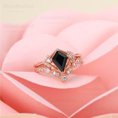 a close up view of a black diamond ring on top of a pink rose petals