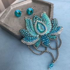 a blue flower brooch and earring set sitting on top of a metal tray