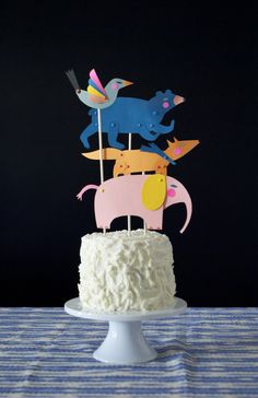 a cake with frosting and paper animals on top, sitting on a blue table cloth