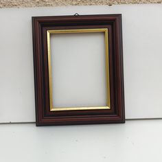 a brown and gold frame hanging on the side of a white wall next to a black cat