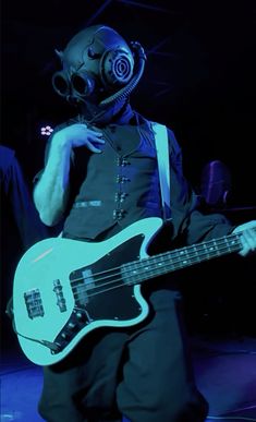 a man wearing a gas mask and holding a guitar in front of him on stage