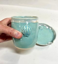 a hand holding a blue cup with a shell on it