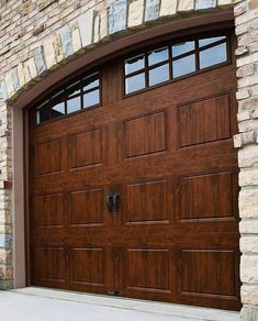 a brown garage door with two windows in front of a brick wall and stone pillars