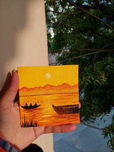 a person holding up a small piece of art that looks like two boats in the water