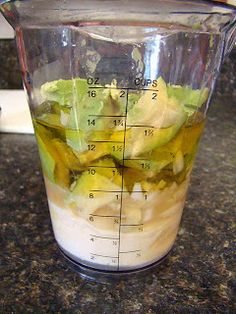 a blender filled with green and yellow vegetables on top of a countertop next to a measuring cup