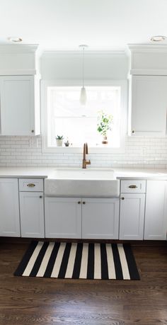 a kitchen with white cabinets and black and white striped rug on the wooden flooring