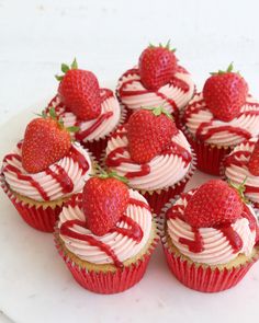 cupcakes with white frosting and strawberries are arranged on a platter