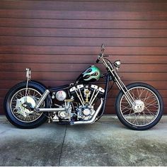 a black motorcycle parked in front of a garage door next to a wooden wall with a green flame on it