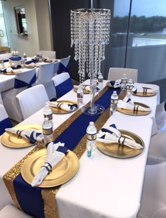 the table is set with blue and white linens, gold plates, silverware, and crystal chandelier