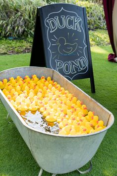 a metal tub filled with lots of oranges next to a chalkboard sign that says duck pond