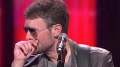 a man with sunglasses on sitting in front of a microphone and wearing a leather jacket