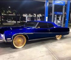 a blue car with gold rims parked in front of a gas station at night