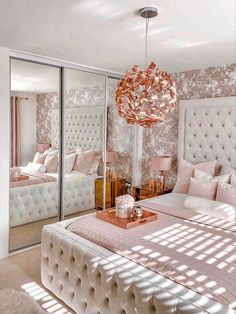 a large white bed sitting in a bedroom next to a mirrored wall and a chandelier