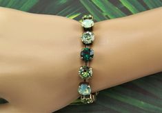 "Shades of opal, green and lavender are displayed in this sparkling Swarovski cup chain bracelet. Each carefully hand set 8mm (39ss) crystal is held with four prongs in an antique bronze 15 cup bracelet, closed with a lobster claw clasp. The pale green opals are complimented with peridot and emerald crystals, intermingled with chrysolite crystals that shimmer pale green. These 39ss chatons are set in this nickle free metal, bronze toned bracelet. A 2\" extender chain finished with an emerald Swa Green Bracelets With Sparkling Stones As Gift, Green Bracelets With Sparkling Stones For Gift, Green Crystal Bracelets With Sparkling Stones, Elegant Adjustable Green Crystal Bracelet, Green Crystal Round Bracelets, Green Crystal Bracelet With Rhinestones, Swarovski Green Bracelet, Green Crystal Bracelet, Hand-strung Green Round Crystal Bracelet