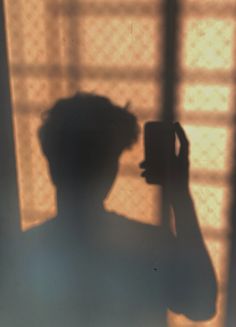 the shadow of a person holding a camera in front of a window with sheer curtains