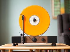 an orange record player sitting on top of a wooden table next to a book shelf