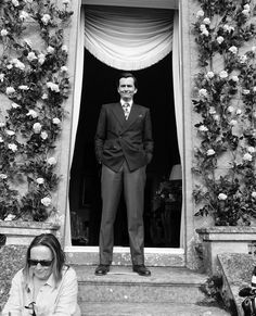 a man in a suit and tie standing at the entrance to a building with flowers on it