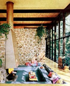 a living room filled with furniture next to a stone wall covered in plants and windows