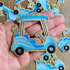 a hand is holding some blue and black embroidered patches with tractors on them in front of a wooden table