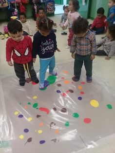 several children are standing on a sheet of plastic in a room with many other kids