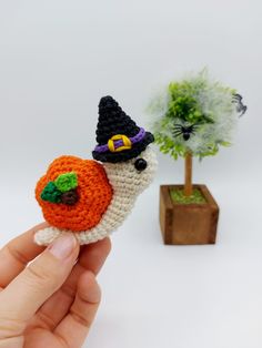 a hand holding a tiny crocheted halloween decoration next to a potted tree